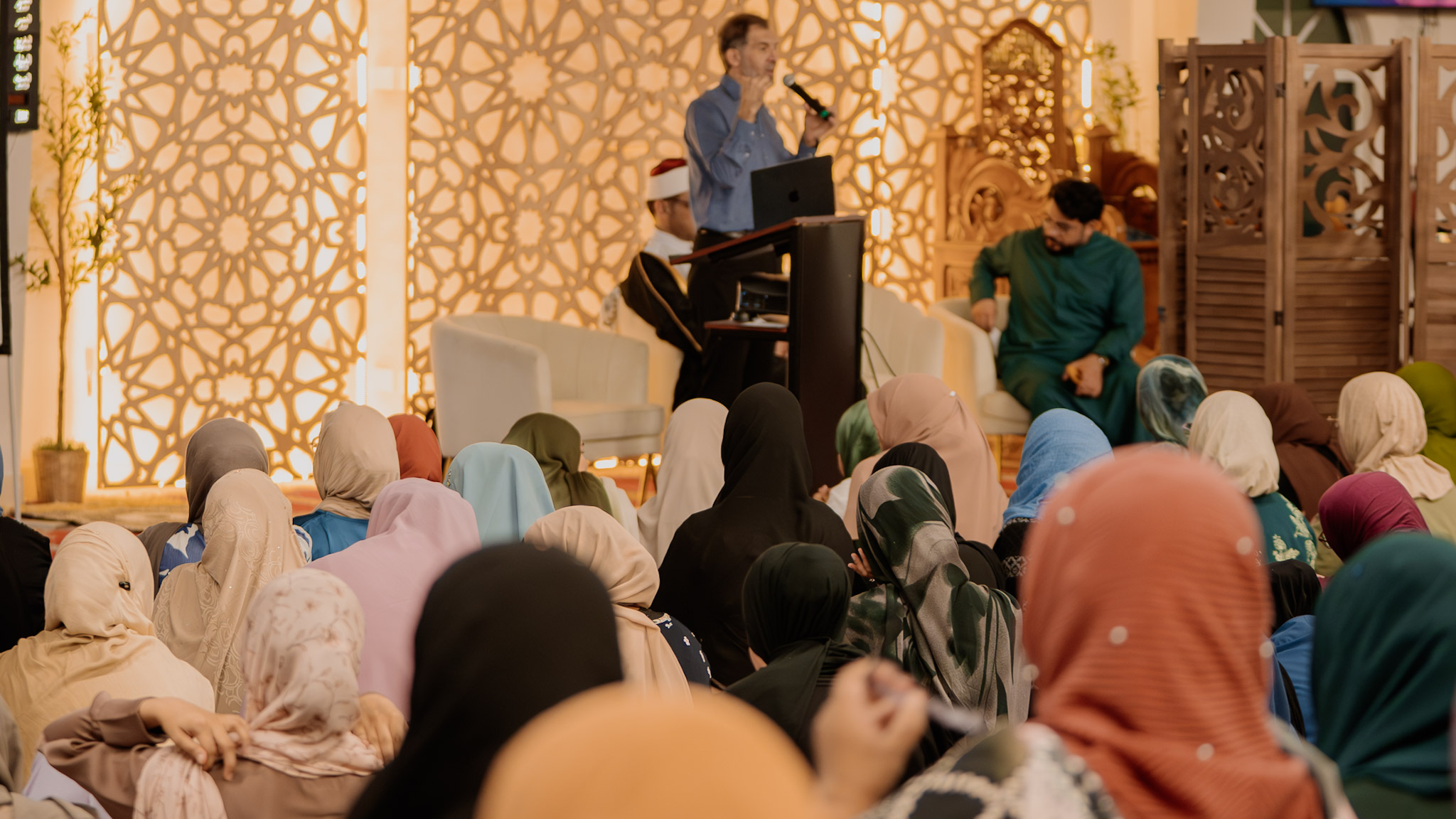 Audience in pastel hijabs against a backlit lattice at IFFS